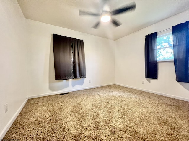 carpeted spare room featuring ceiling fan, visible vents, and baseboards