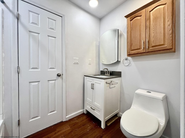 half bath with vanity, baseboards, wood finished floors, and toilet