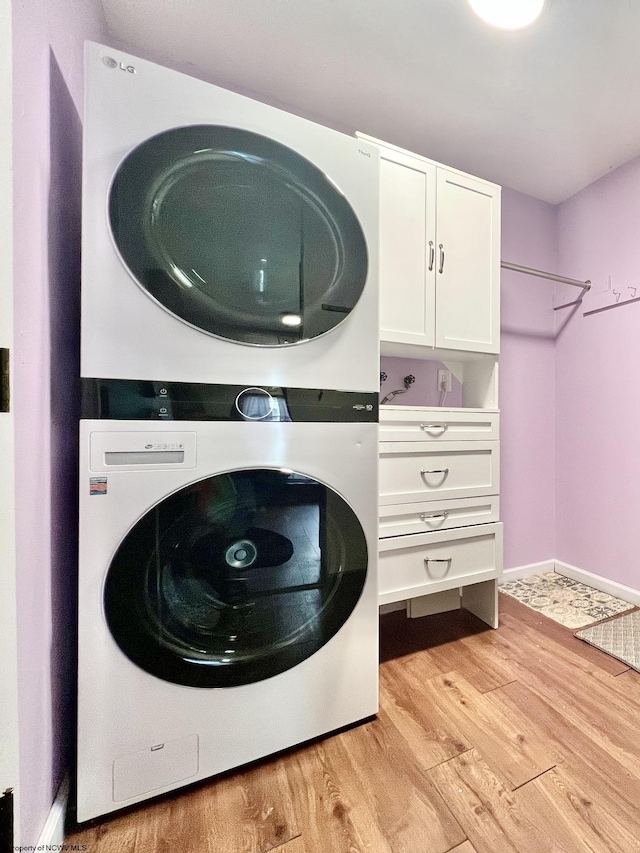 clothes washing area with light wood-style floors, baseboards, and stacked washer / drying machine