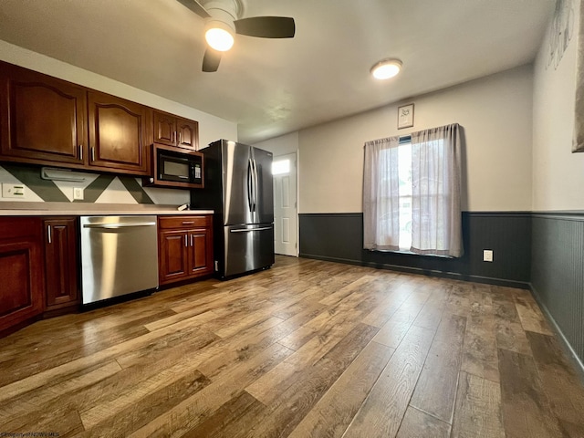 kitchen with appliances with stainless steel finishes, a ceiling fan, wainscoting, and hardwood / wood-style floors