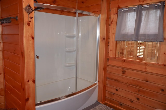 bathroom featuring wood walls and shower / bath combination with glass door