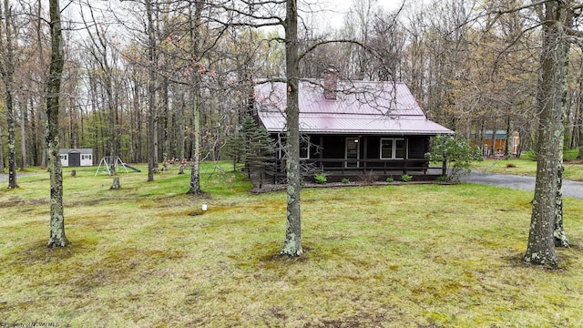 chalet / cabin with covered porch, metal roof, a chimney, and a front yard