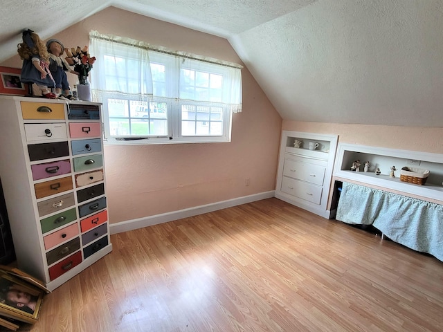 additional living space with a textured ceiling, baseboards, lofted ceiling, and light wood-style floors