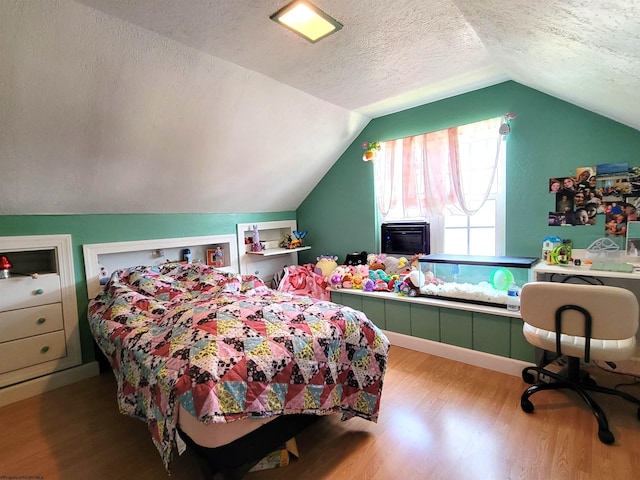 bedroom with lofted ceiling, a textured ceiling, and wood finished floors
