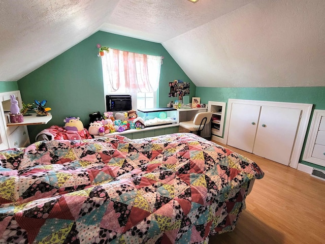 bedroom with light wood-style flooring, a textured ceiling, and vaulted ceiling