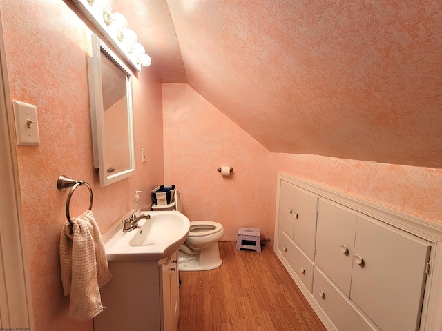 bathroom featuring vaulted ceiling, toilet, a textured wall, and wood finished floors