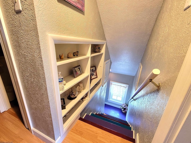 stairway with a textured ceiling, wood finished floors, and a textured wall
