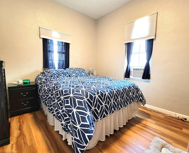 bedroom with a textured wall, baseboards, cooling unit, and wood finished floors