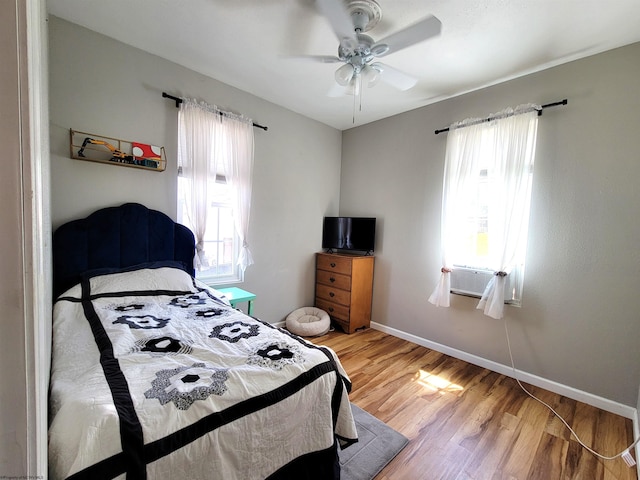 bedroom with baseboards, multiple windows, ceiling fan, and wood finished floors