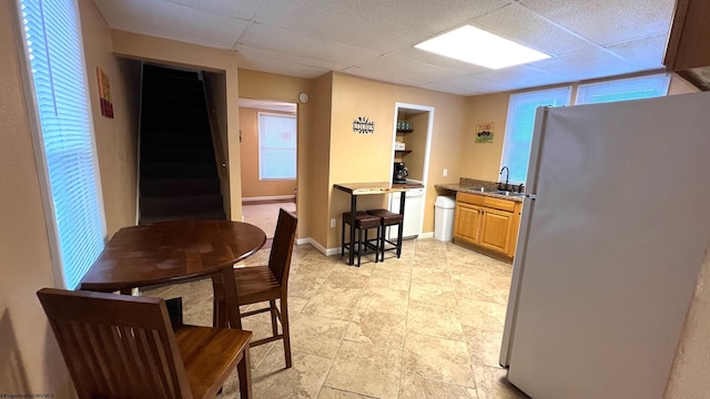 kitchen with freestanding refrigerator, a drop ceiling, baseboards, and a sink
