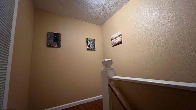 corridor with a textured ceiling, baseboards, and dark wood-style floors