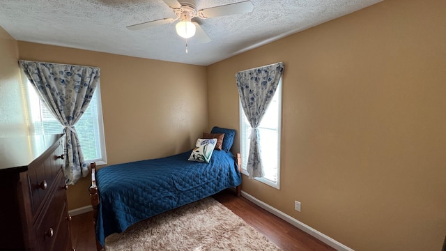 bedroom featuring baseboards, ceiling fan, a textured ceiling, and wood finished floors