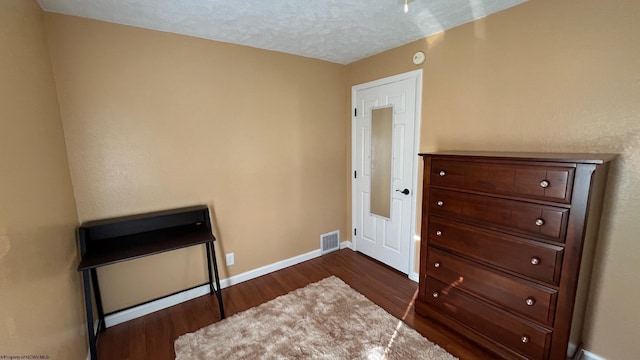 bedroom with baseboards, dark wood finished floors, visible vents, and a textured ceiling