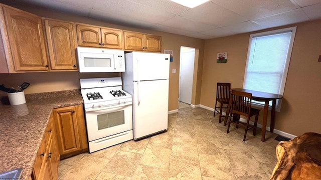 kitchen featuring baseboards, a drop ceiling, white appliances, and brown cabinets