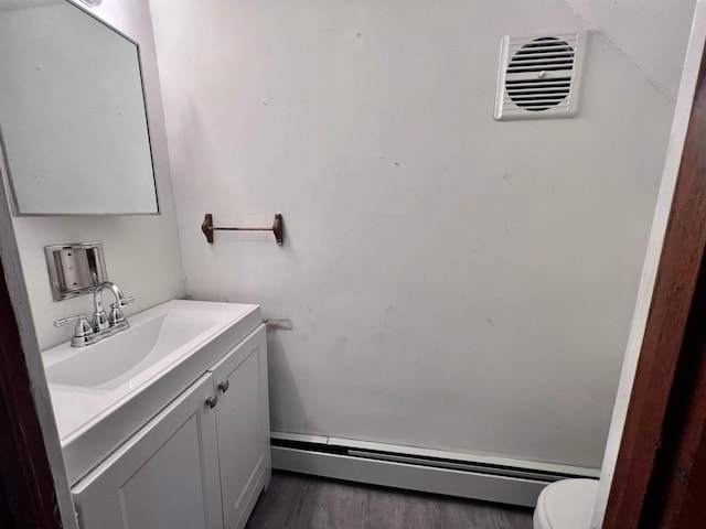 bathroom featuring toilet, wood finished floors, vanity, visible vents, and baseboard heating