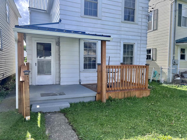 property entrance with fence, a wooden deck, and a lawn