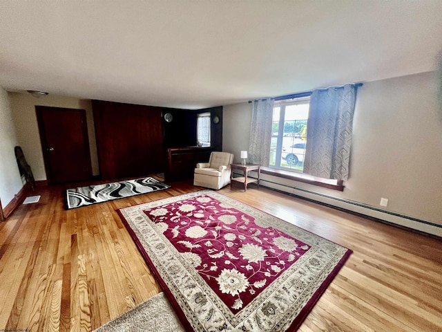 living area with visible vents, wood finished floors, and a baseboard heating unit