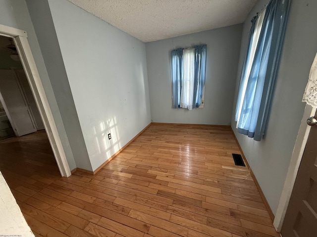 unfurnished bedroom featuring baseboards, light wood-style floors, visible vents, and a textured ceiling