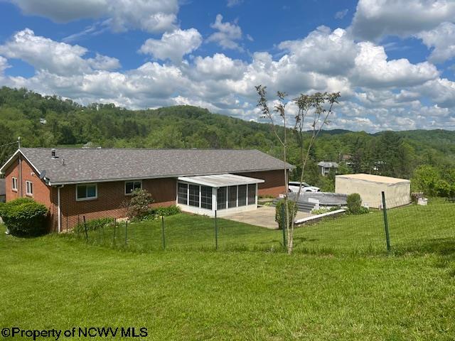 rear view of property with a sunroom, a wooded view, a lawn, and brick siding