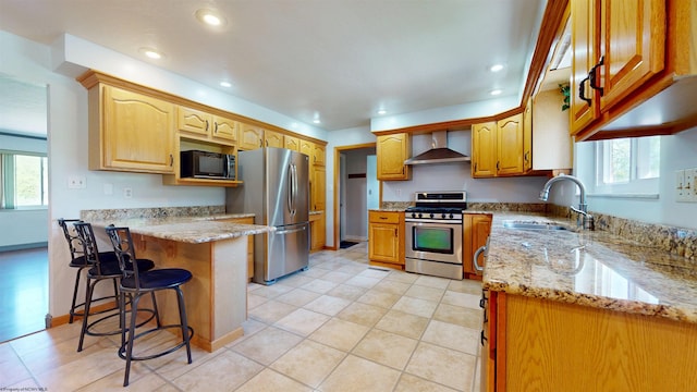 kitchen featuring stainless steel appliances, wall chimney range hood, a sink, a peninsula, and light stone counters