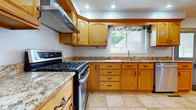 kitchen featuring appliances with stainless steel finishes, ventilation hood, a sink, light stone countertops, and brown cabinets