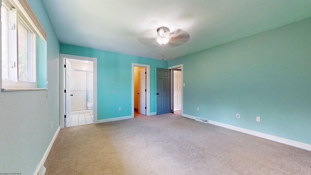 unfurnished bedroom with carpet floors, baseboards, ensuite bathroom, a walk in closet, and a ceiling fan