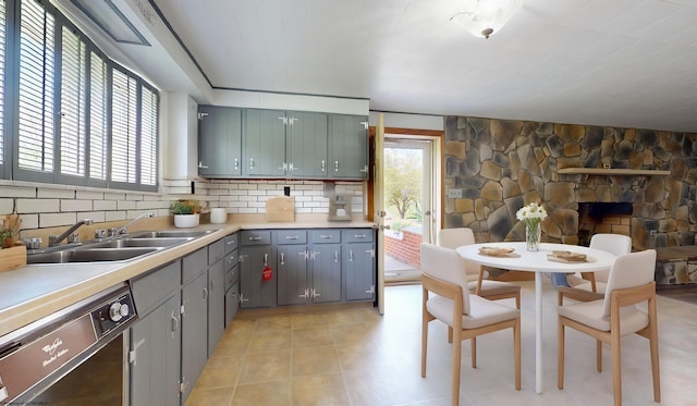 kitchen featuring a sink, dishwasher, light countertops, backsplash, and gray cabinets