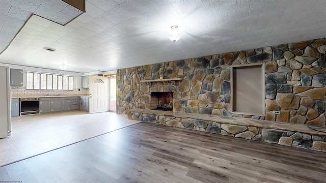 unfurnished living room with a stone fireplace, light wood-style floors, and a sink