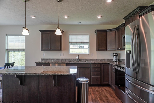 kitchen featuring stainless steel appliances, a sink, dark wood-style floors, dark brown cabinets, and a breakfast bar area