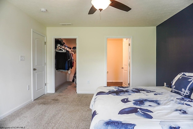 carpeted bedroom with a walk in closet, baseboards, ensuite bathroom, a closet, and a ceiling fan