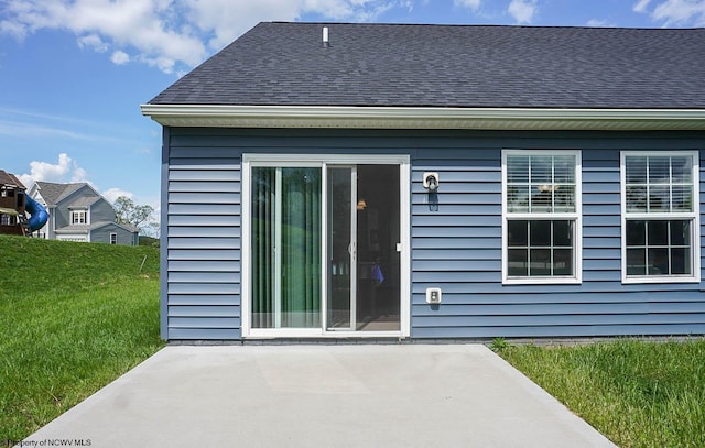back of property with a patio area, roof with shingles, and a lawn