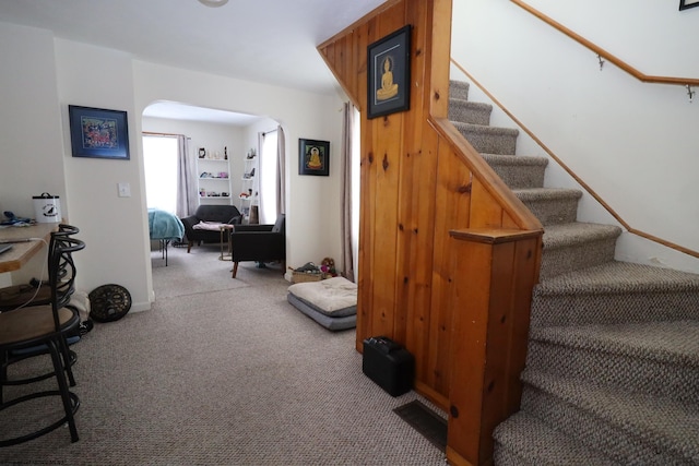 stairway featuring arched walkways and carpet floors