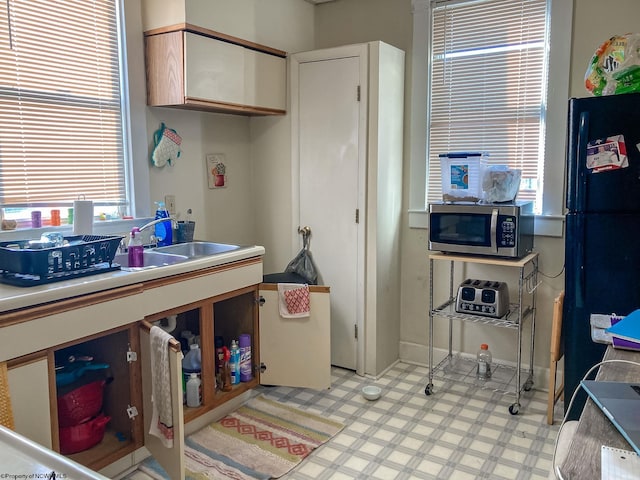 kitchen featuring stainless steel microwave, light flooring, a sink, freestanding refrigerator, and light countertops