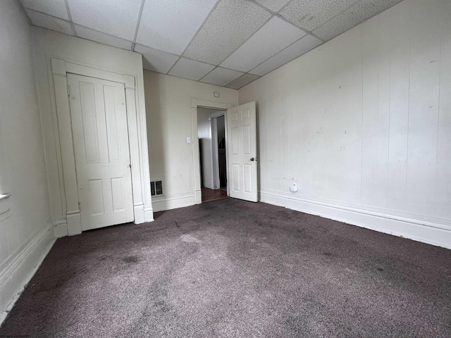 unfurnished bedroom featuring carpet flooring, a paneled ceiling, and baseboards