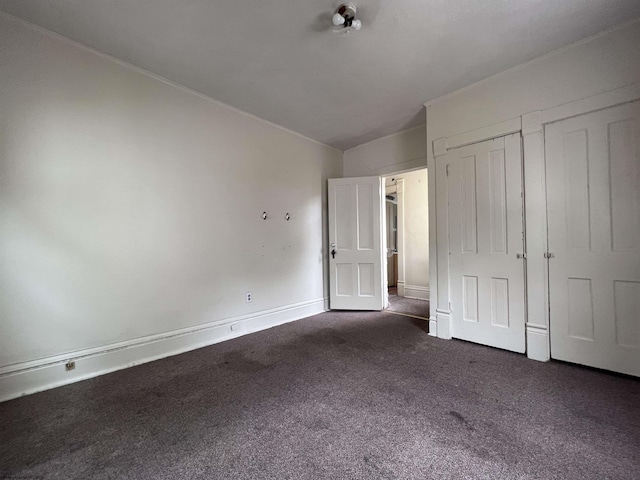 unfurnished bedroom featuring dark colored carpet, baseboards, and multiple closets