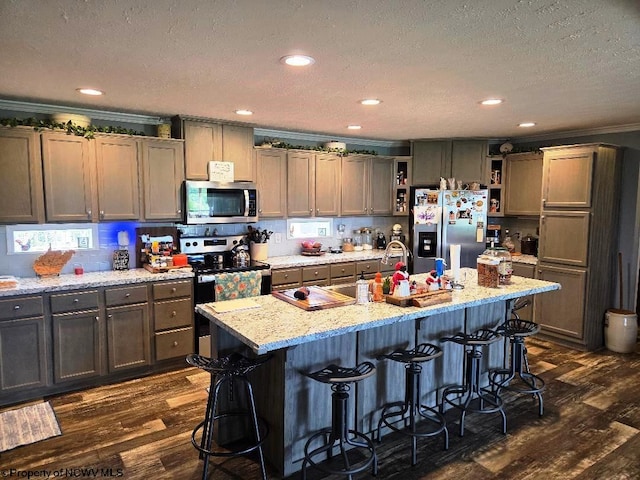 kitchen with appliances with stainless steel finishes, open shelves, dark wood-style flooring, a textured ceiling, and a breakfast bar