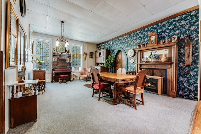 carpeted dining room with wallpapered walls, a glass covered fireplace, a drop ceiling, and a chandelier