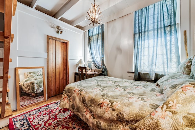 bedroom with a chandelier, beam ceiling, wood finished floors, and a closet