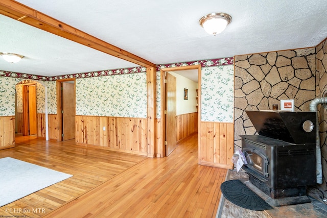 22 N Euclid Ave, Thomas, WV 26292 - unfurnished living room with a wood stove, wood-type flooring, wallpapered walls, wainscoting, and a textured ceiling