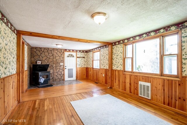 22 N Euclid Ave, Thomas, WV 26292 - unfurnished living room featuring a textured ceiling, light wood-style flooring, wainscoting, a wood stove, and wallpapered walls