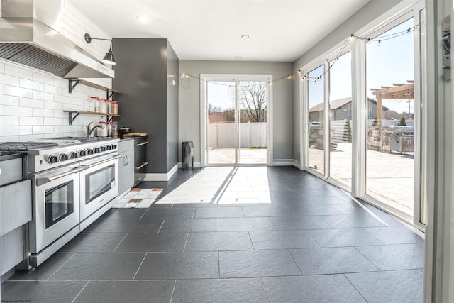 kitchen featuring double oven range, exhaust hood, open shelves, tasteful backsplash, and baseboards