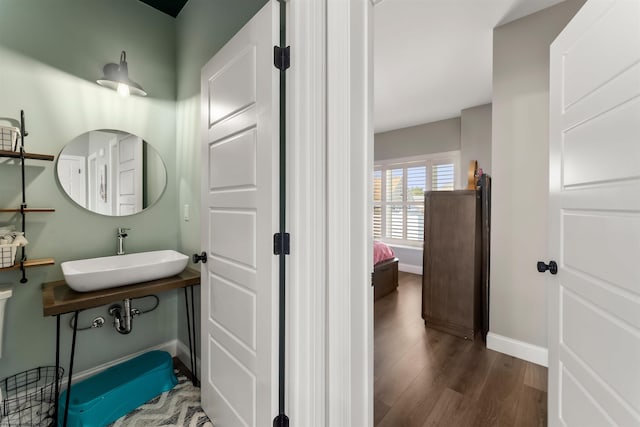 ensuite bathroom with a sink, wood finished floors, and baseboards
