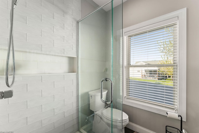 bathroom featuring a tile shower, toilet, plenty of natural light, and baseboards
