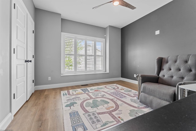 living area featuring a ceiling fan, light wood-style floors, and baseboards