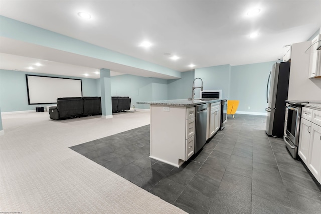 kitchen featuring appliances with stainless steel finishes, an island with sink, baseboards, white cabinetry, and open floor plan