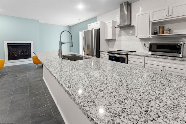 kitchen featuring wall chimney exhaust hood, appliances with stainless steel finishes, a sink, white cabinets, and light stone countertops