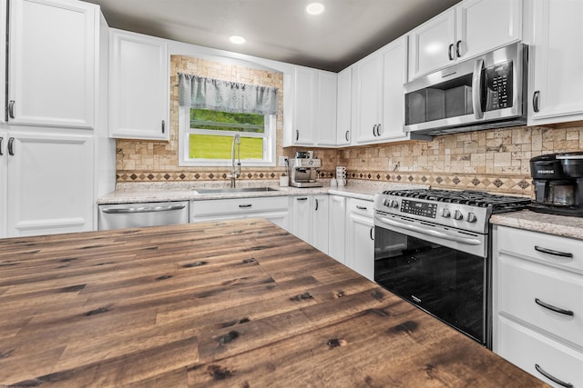 kitchen featuring appliances with stainless steel finishes, butcher block countertops, a sink, tasteful backsplash, and recessed lighting