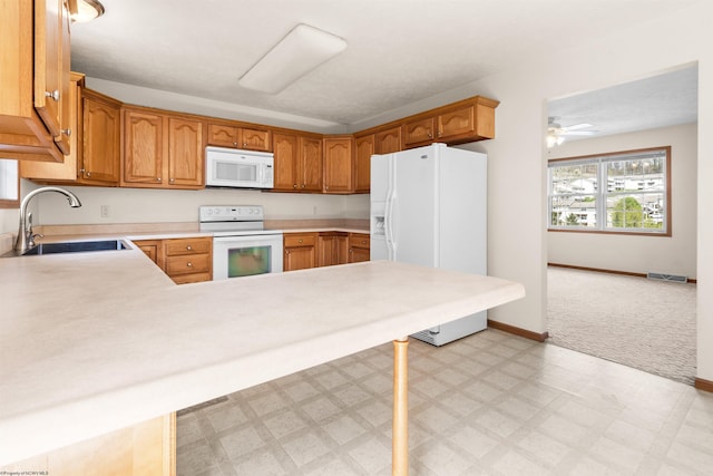 kitchen featuring white appliances, a sink, light flooring, light countertops, and a peninsula