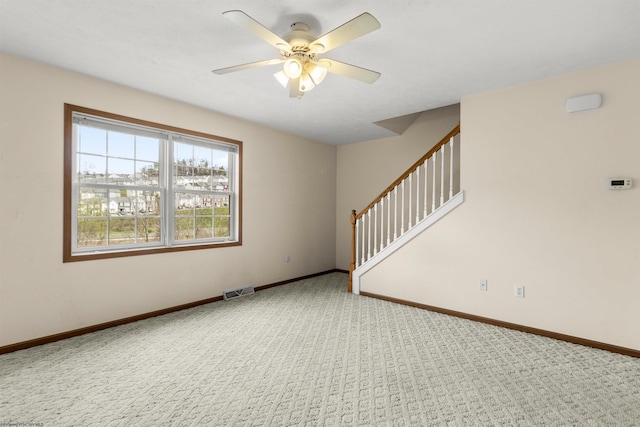carpeted spare room with ceiling fan, baseboards, and stairs