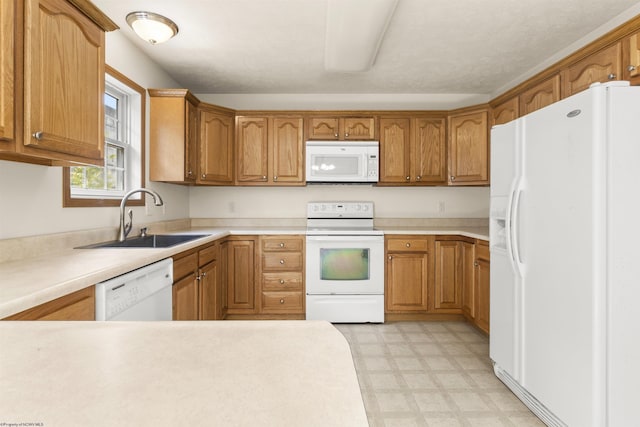 kitchen featuring white appliances, a sink, light floors, light countertops, and brown cabinetry